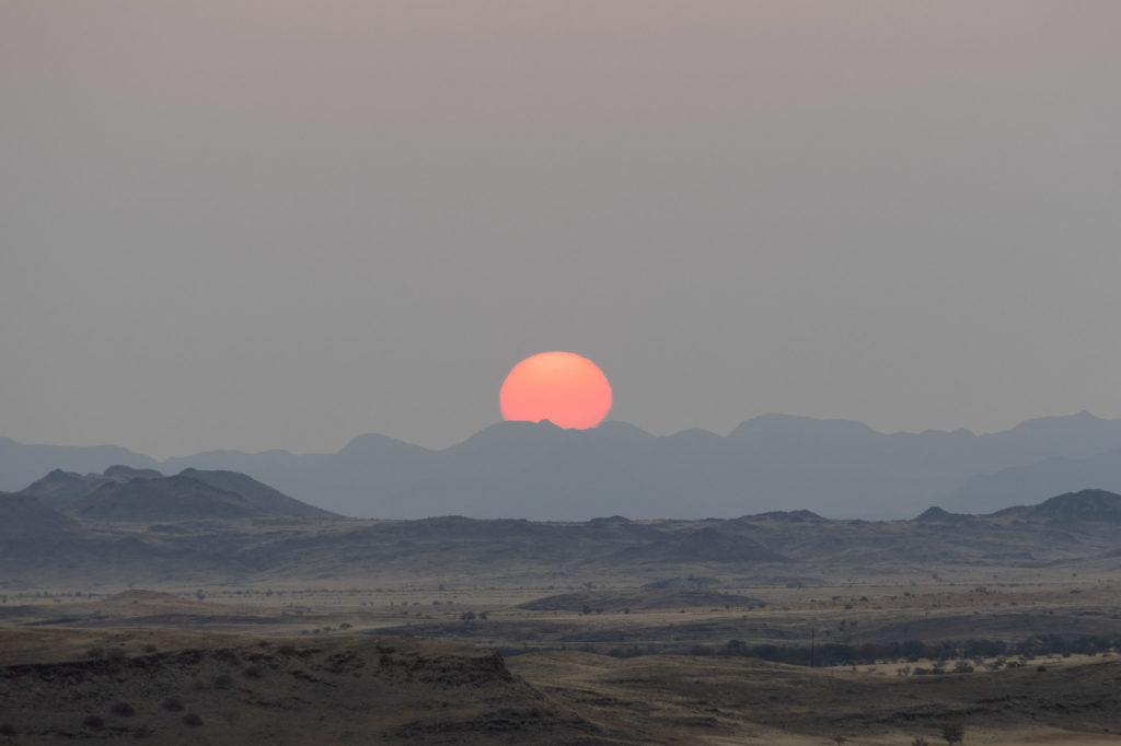 A n image of a full organge sun dipping behind a range of shadow mountains. Image used to represent books catagorised asbeing wide and expansive.